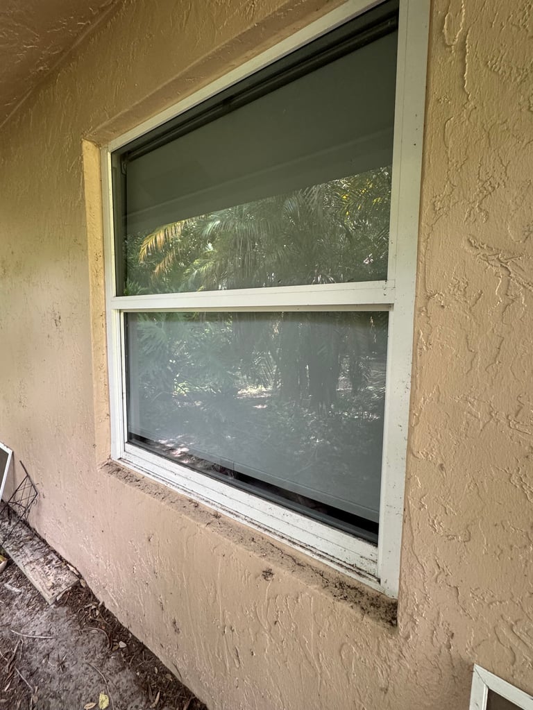 Sliding window with dark screens on beige stucco building exterior showing trees and landscape beyond