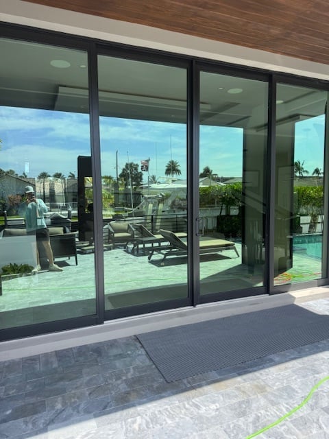 Modern glass sliding doors opening to a rooftop terrace with seating, overlooking a city skyline with palm trees