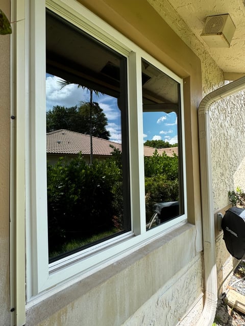 Freshly cleaned sliding glass doors with white frames on a cream-colored home reflecting green hedges and South Florida sky
