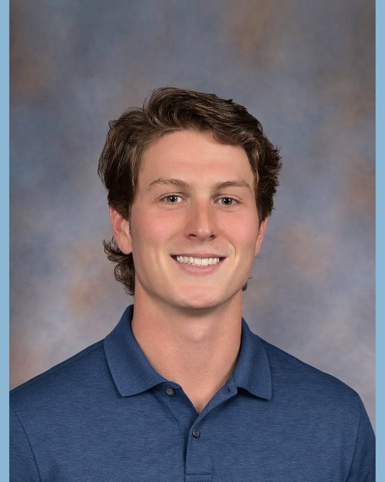 Young man with dark hair smiling at camera, wearing a blue polo shirt against a muted blue-gray background