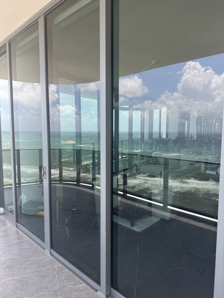 Modern high-rise balcony with floor-to-ceiling glass doors overlooking a coastal city skyline and ocean under blue sky with clouds