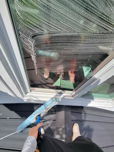 Person cleaning a window with a blue squeegee and mesh screening visible above