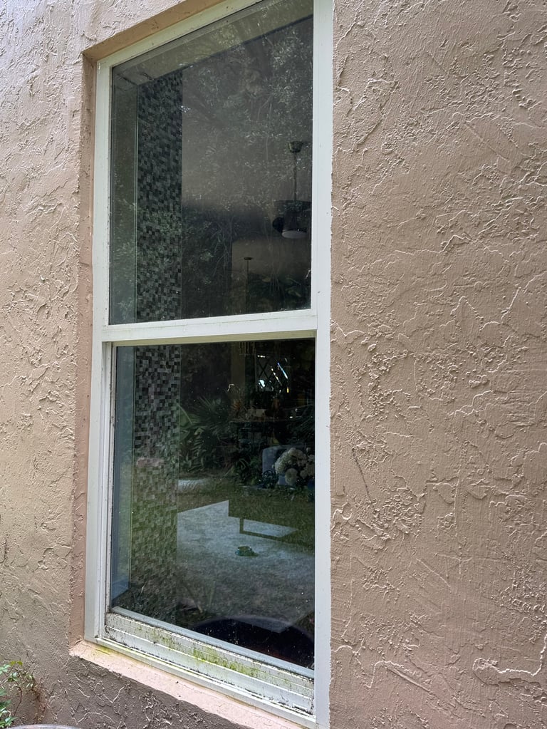 A tall vertical window with white frame on a textured stucco wall, showing a tiled interior wall through the glass.